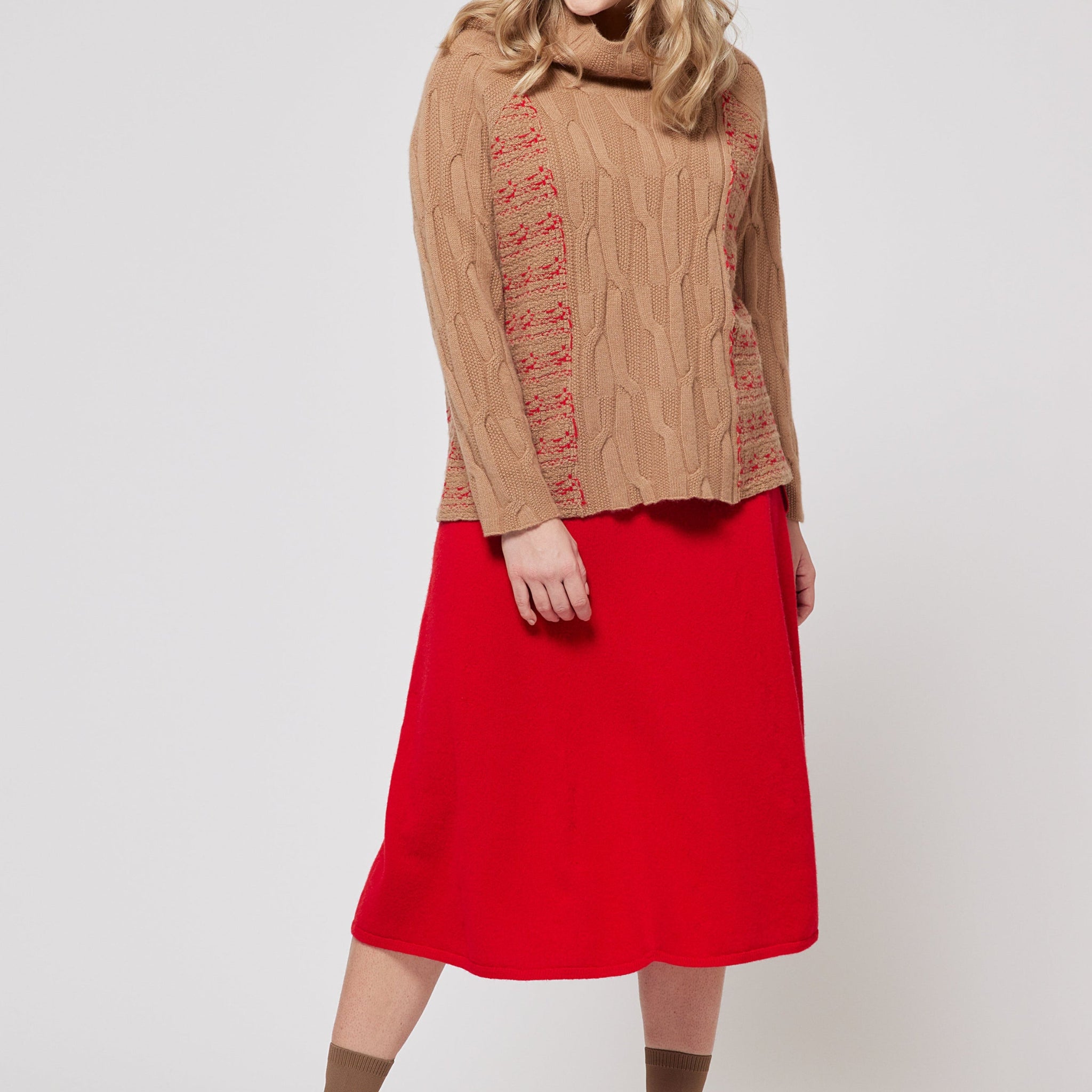 Woman wearing a brown sweater with red patterns and a red skirt on a white background